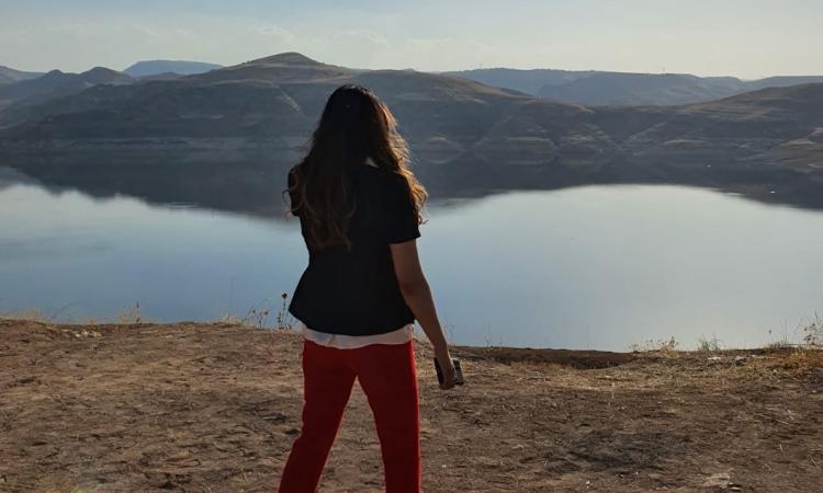A woman stands outside in front of a lake
